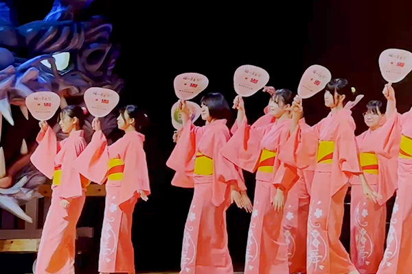 龍の音楽祭の舞台でうちわを手に踊りを披露する生徒たち