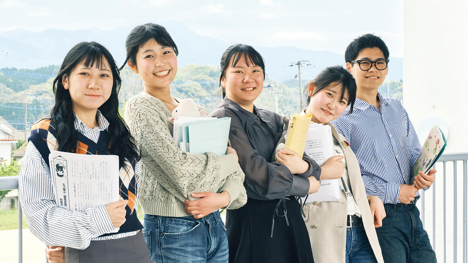 校舎のテラスで教材を持つ生徒と教員